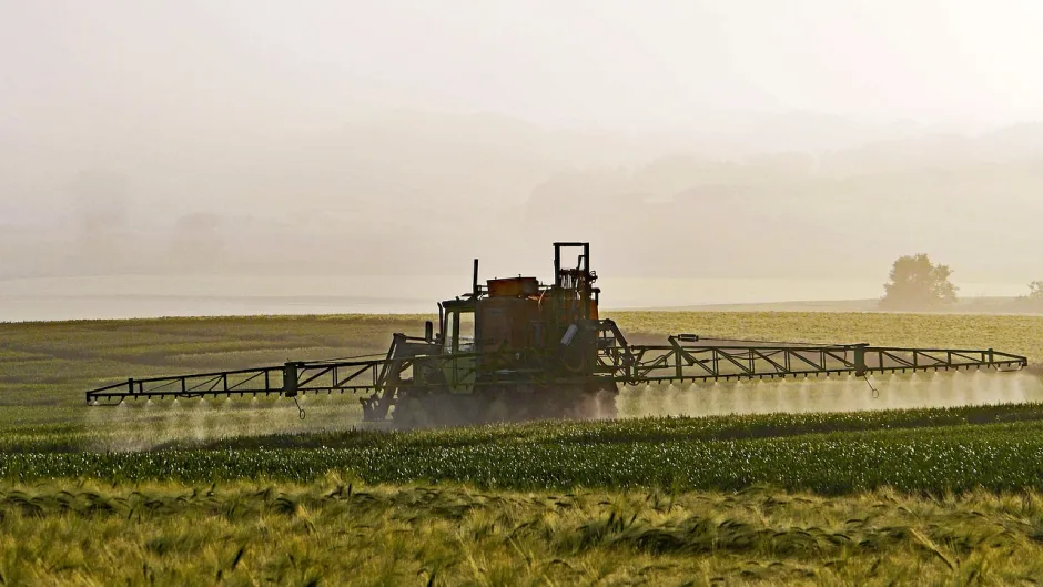 Blick auf ein landwirtschaftliches Fahrzeug, das ein Feld besprüht.